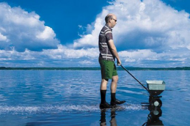 A person walking on a body of water pushing a fertilizer spreader.